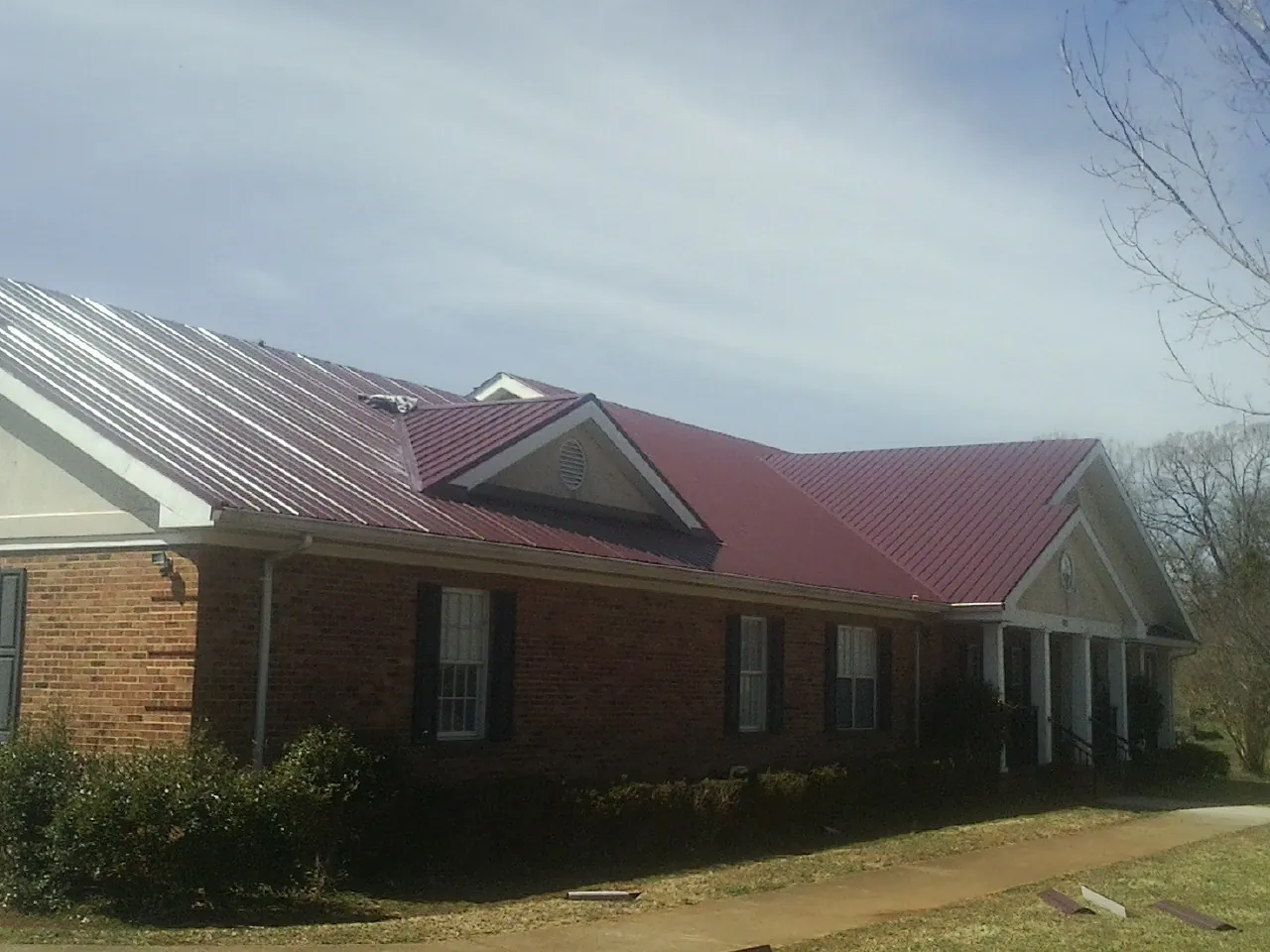 Red metal roof with gabled entries on a long brick building, from a Hail Damage Roof Repair job in Roscoe