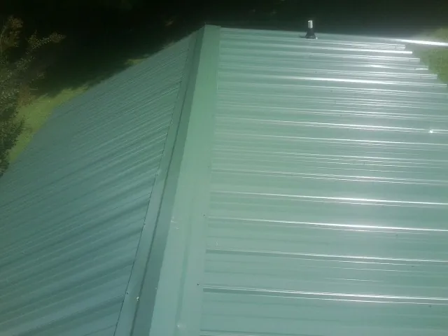 New green metal panels meeting at the ridge of a roof — Flat Roof Repair work by our crew in Roscoe